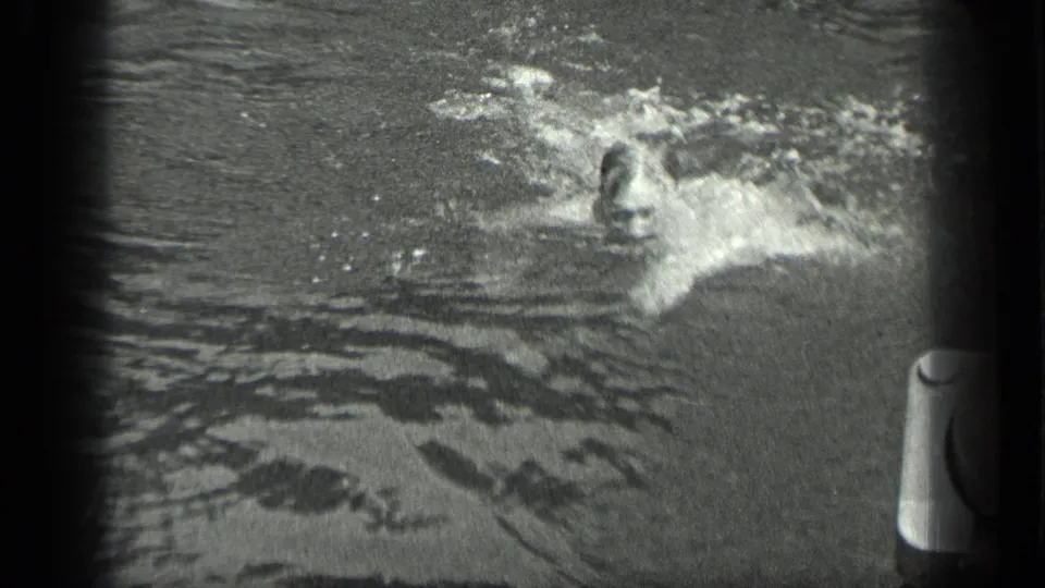 A swimmer moves through Long Lake water in 1939 home-movie footage, creating bright splashes near a dock or boat edge.