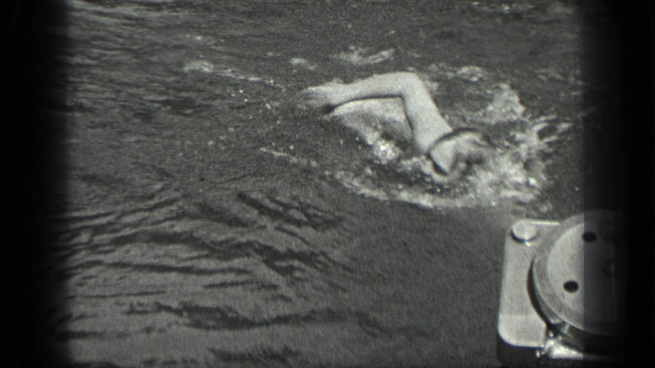 A swimmer in dark water raises an arm during a stroke near dock or boat hardware at Long Lake, Canada.
