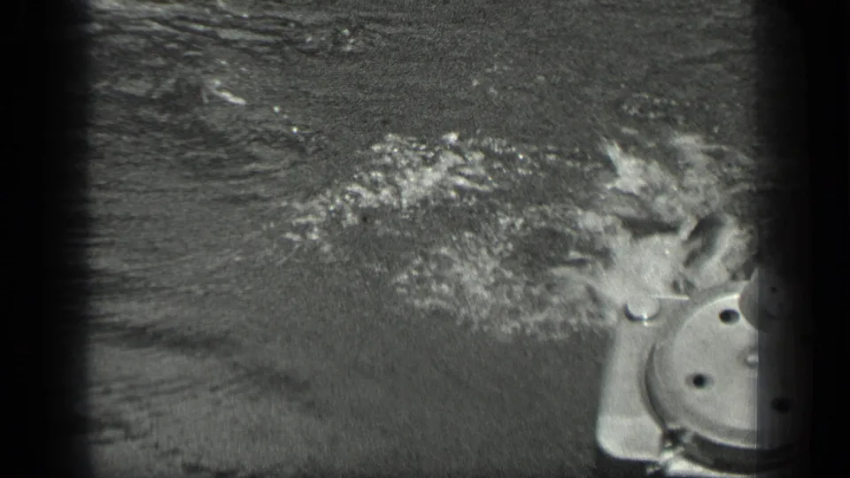 The swimmer moves close to visible dock or boat hardware, with water splashing around the head and shoulders.