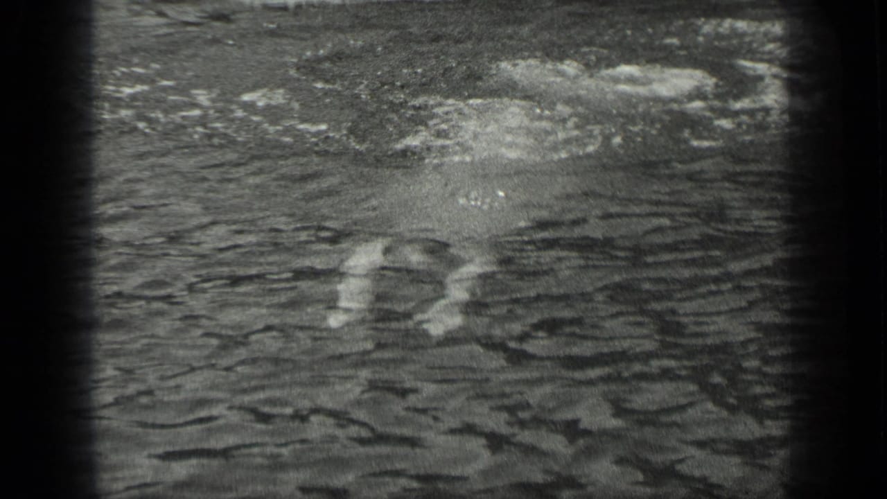 In 1939 Long Lake, Canada footage, a swimmer is partly submerged in rippled water near the camera frame edge.