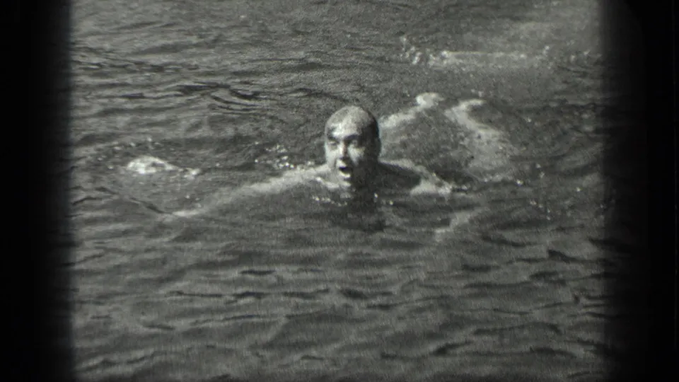 A man swims toward the camera at Long Lake, Canada, with his face above the water and arms extended.