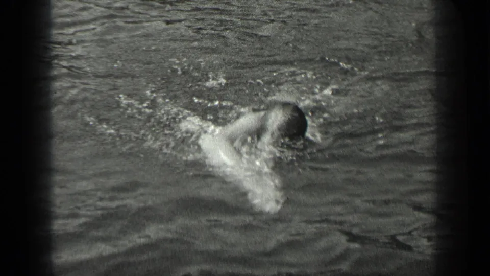 The swimmer dips forward during a stroke, creating splashes in the dark rippled lake water.