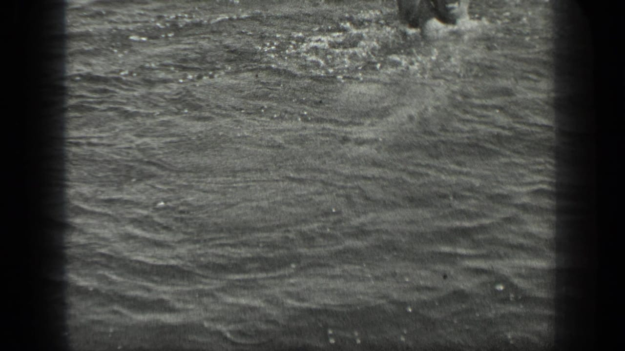 1939 Long Lake, Canada home-movie frame showing a swimmer partly cropped in rippling water with strong 8mm grain.