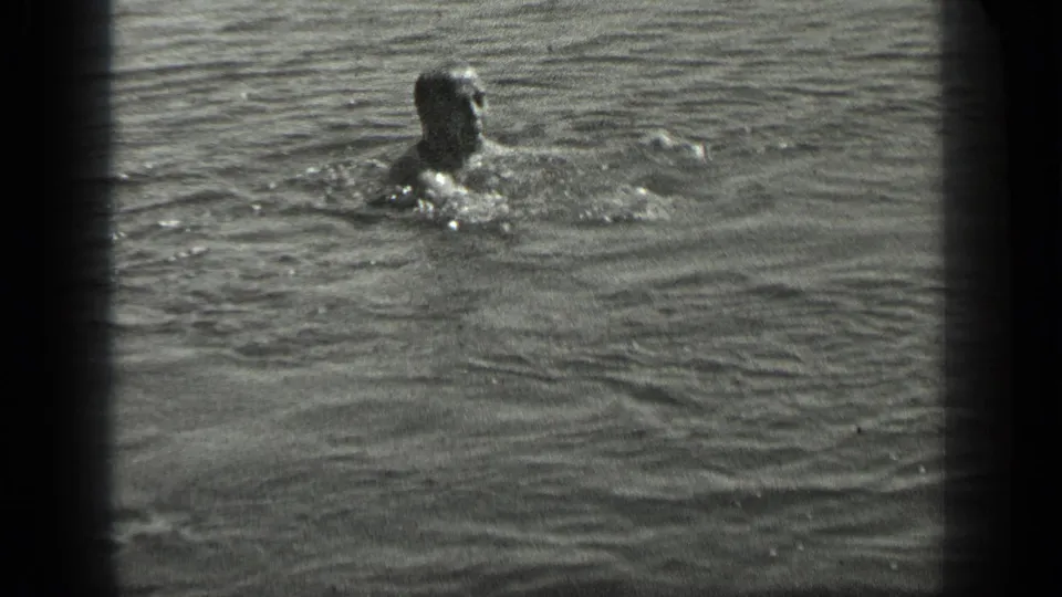 A swimmer at Long Lake, Canada, surfaces in rippling water in a grainy 1939 black-and-white 8mm frame.