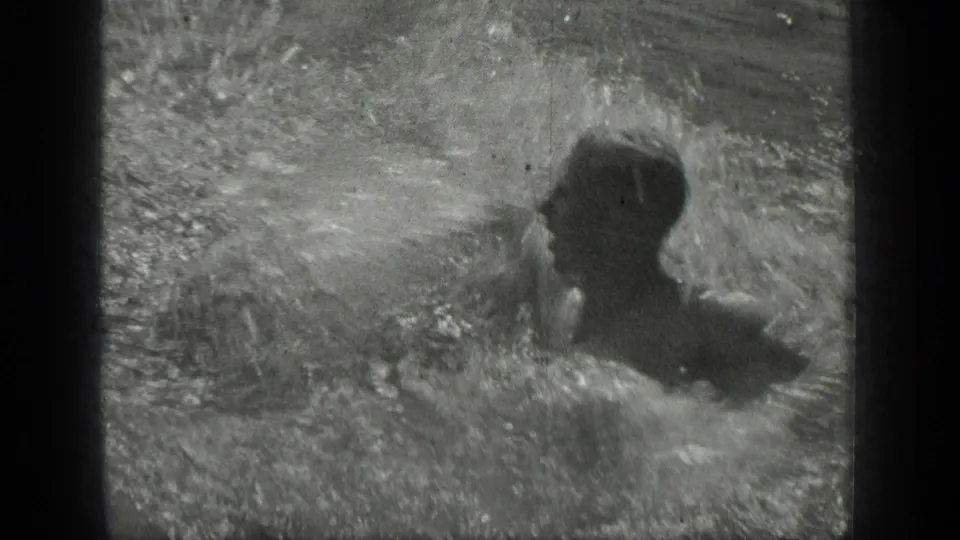 At Long Lake, Canada in the supplied 1939 context, two swimmers splash close together in grainy black-and-white lake footage.