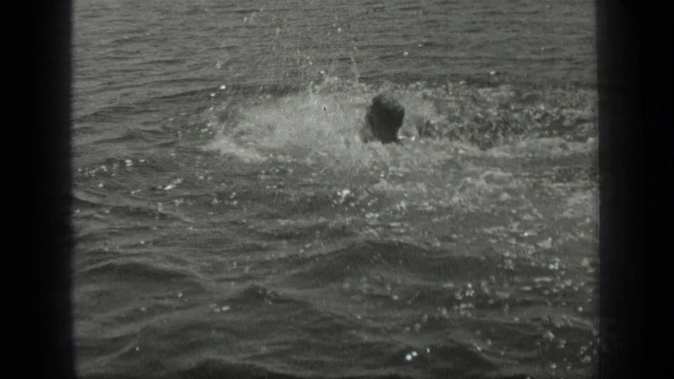 A swimmer appears near a large splash in Long Lake, Canada, while another dark head is faintly visible in the water.
