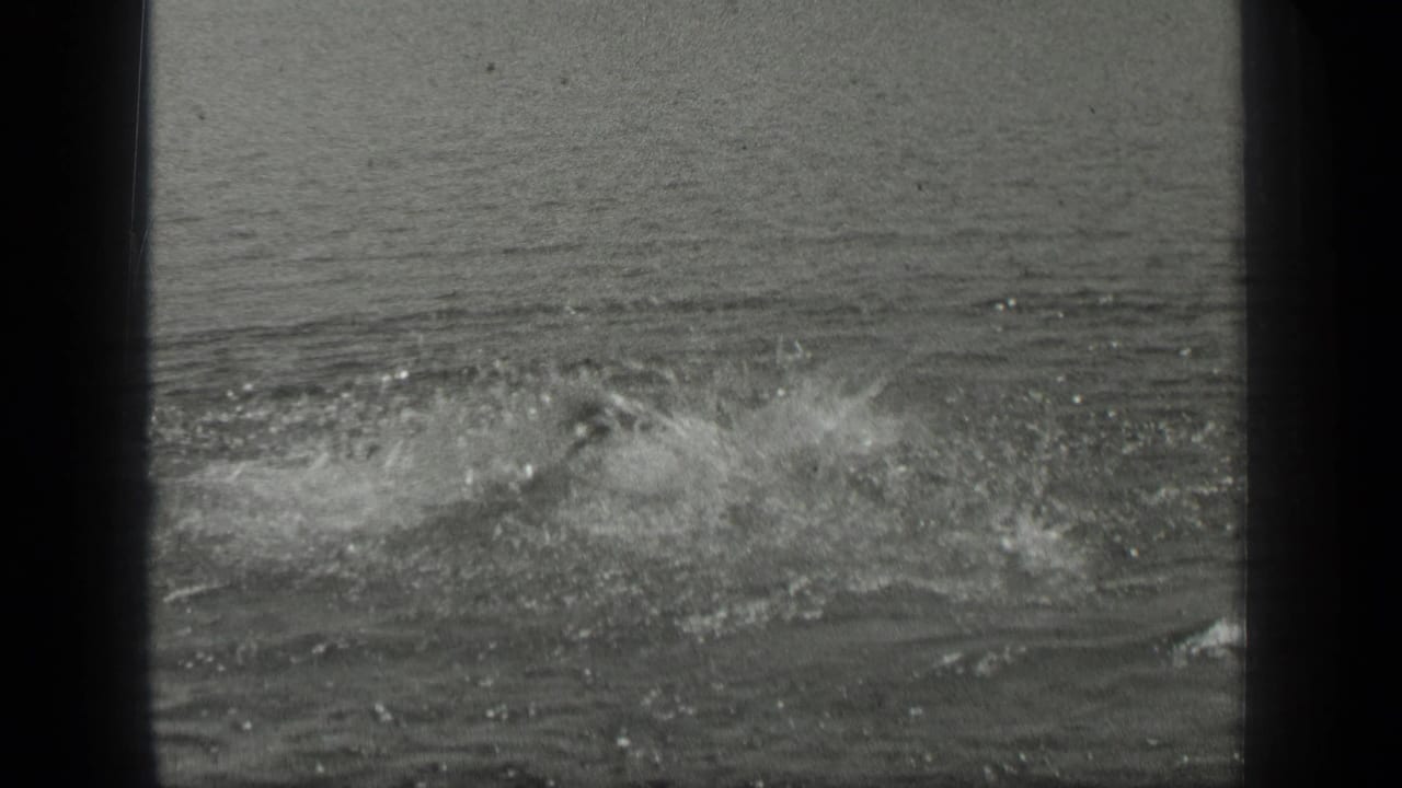 1939 Long Lake frame with a swimmer mostly hidden by spray while the surrounding water ripples outward.