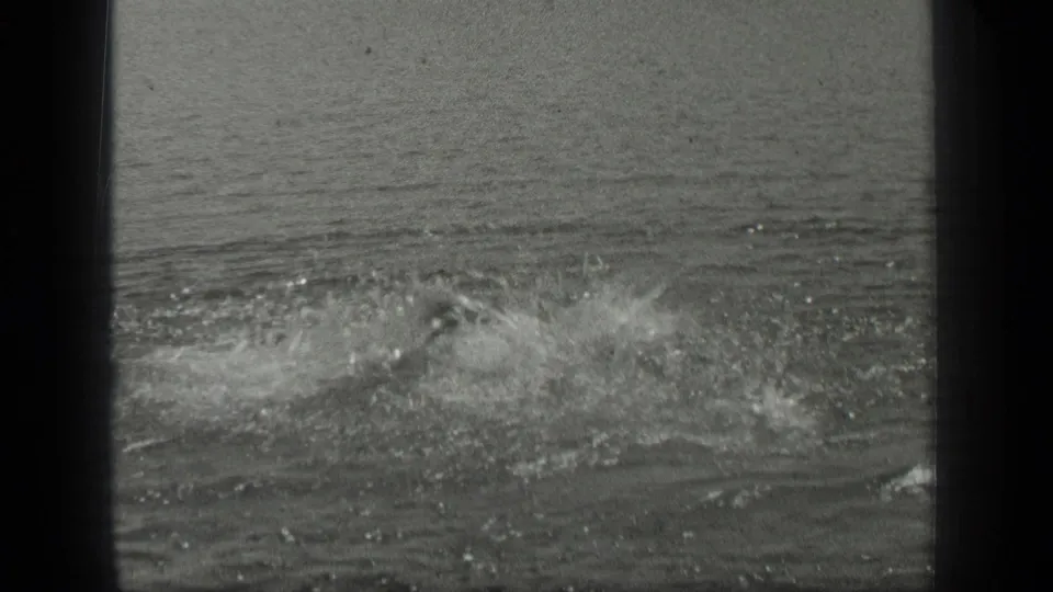 1939 Long Lake frame with a swimmer mostly hidden by spray while the surrounding water ripples outward.