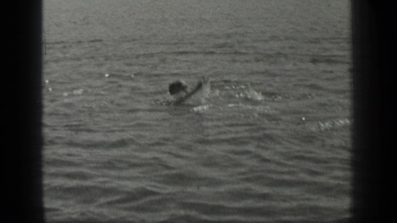 1939 Long Lake frame showing a distant swimmer crossing the water, with one arm raised and small splashes nearby.