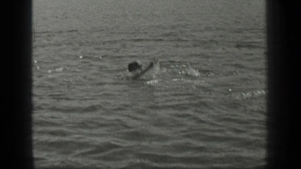 1939 Long Lake frame showing a distant swimmer crossing the water, with one arm raised and small splashes nearby.