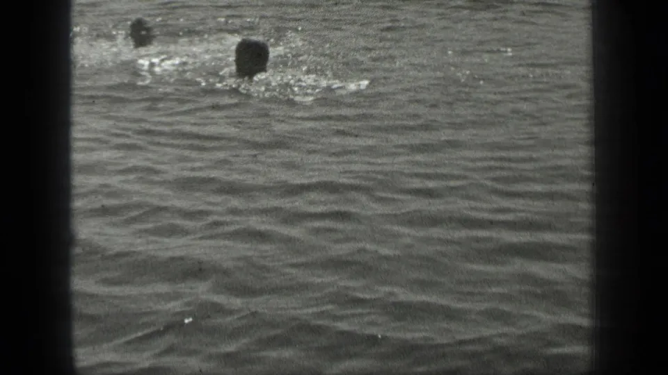 Long Lake frame with one swimmer splashing near the upper right and another distant head in the water.