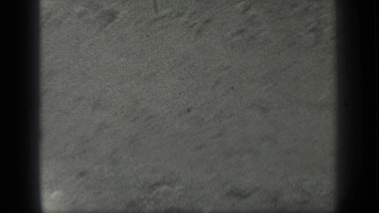 1939 8mm home-movie frame showing a soft, grainy Long Lake water view with faint ripples and sandy bottom texture.