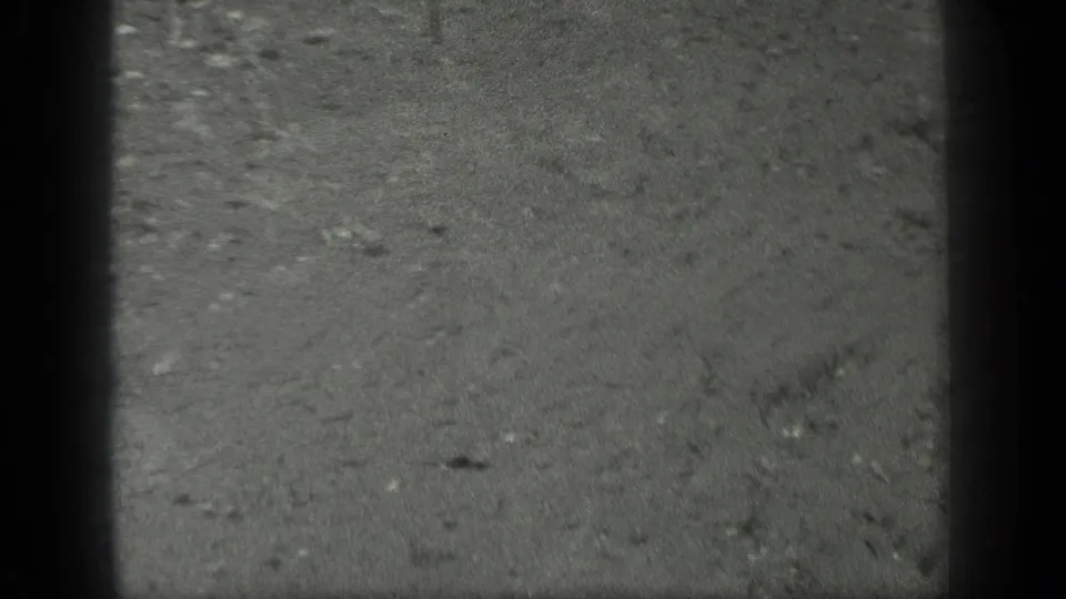 1939 Long Lake, Canada 8mm frame showing rain-marked pavement with faint water streaks, small debris, and soft black-and-white texture.