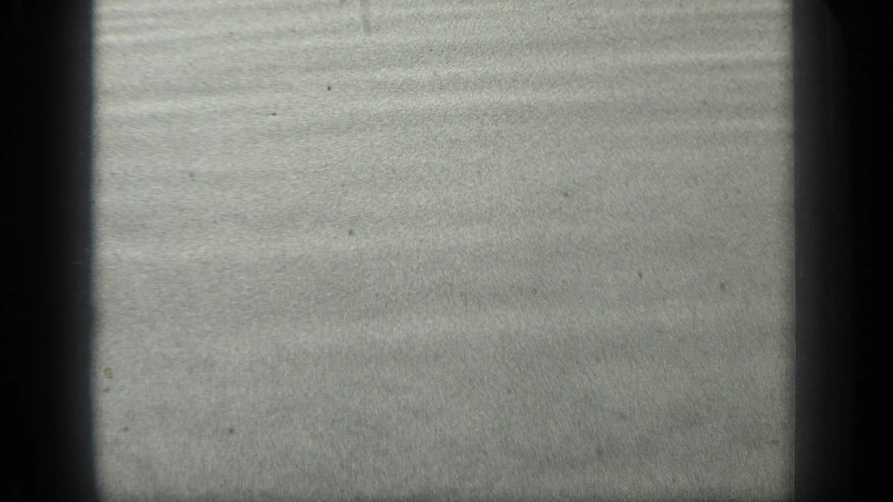 Close 8mm view of Long Lake wet sand or shallow water, showing horizontal ripple lines and visible film wear.