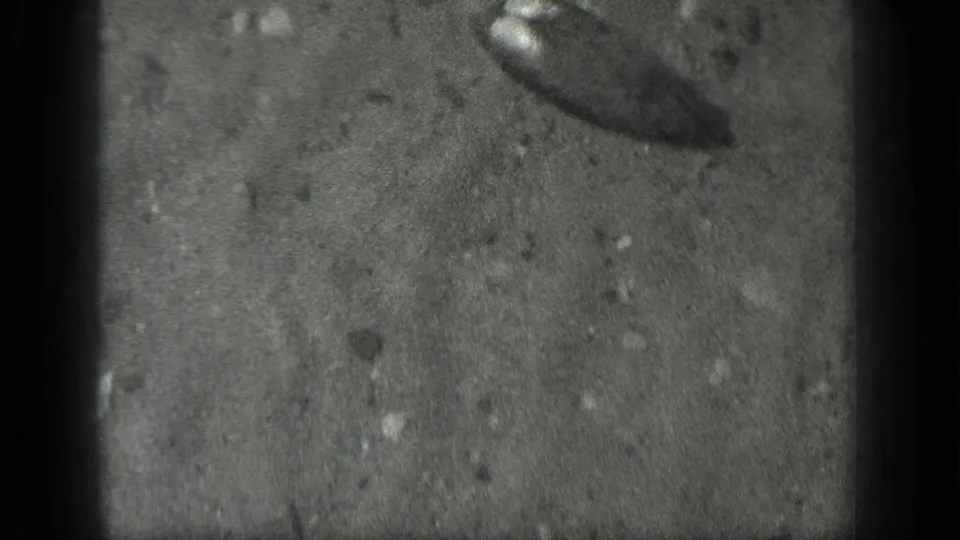 1939 Long Lake, Canada frame showing clear shallow water, sandy lake bottom, small stones, and a dark indistinct object near the edge.