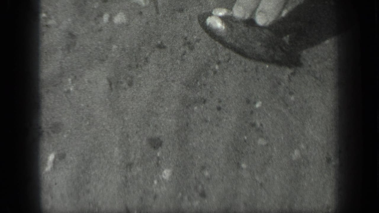 In 1939 Long Lake home-movie footage, a partial hand appears near the top edge over cloudy pond water and sediment.