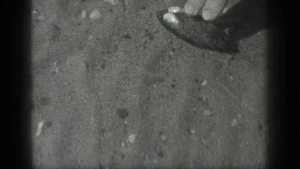 In 1939 Long Lake home-movie footage, a partial hand appears near the top edge over cloudy pond water and sediment.