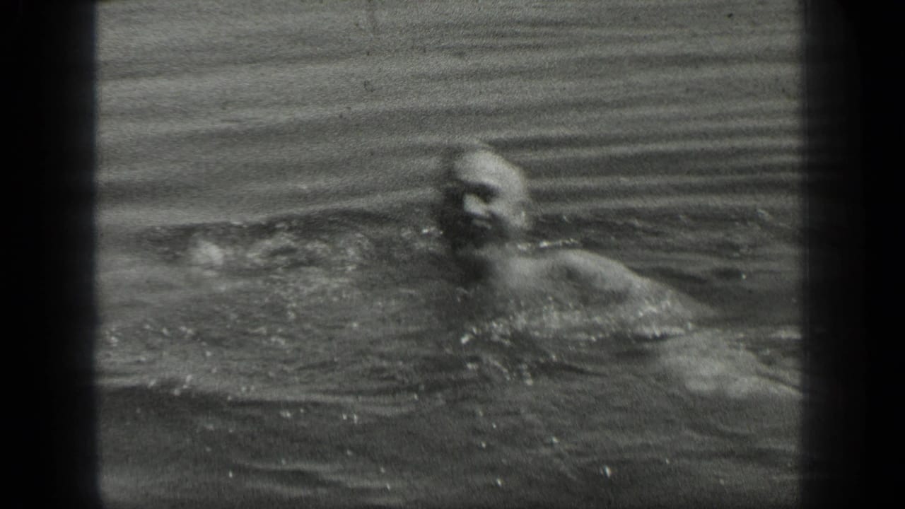 Black-and-white 8mm frame of a man swimming in Long Lake, Canada, with his face and upper body partly visible in the water.