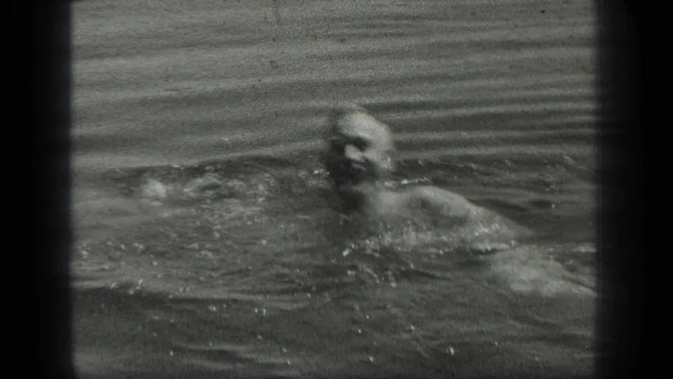 Black-and-white 8mm frame of a man swimming in Long Lake, Canada, with his face and upper body partly visible in the water.