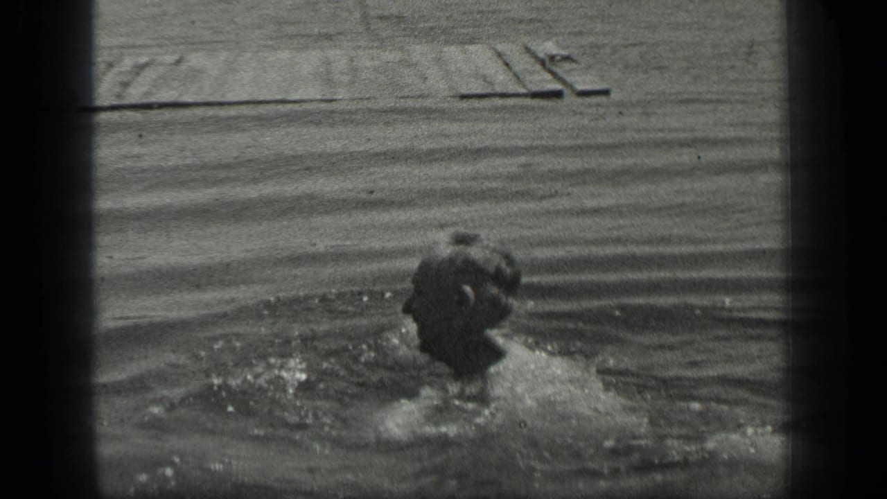 Man swimming in lake water with a wooden pier in the background.