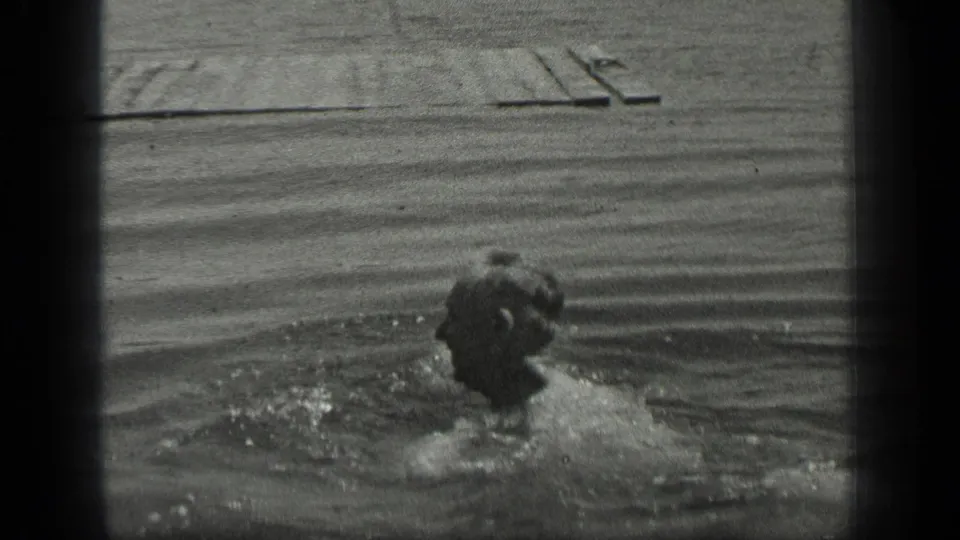 At Long Lake, Canada in 1939, an adult man swims through rippled water with a wooden pier visible behind him.