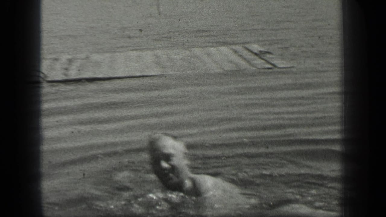The swimmer faces toward the camera in Long Lake, Canada, with the dock and rippled lake surface behind him.