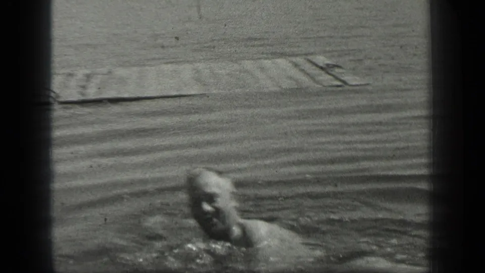 The swimmer faces toward the camera in Long Lake, Canada, with the dock and rippled lake surface behind him.
