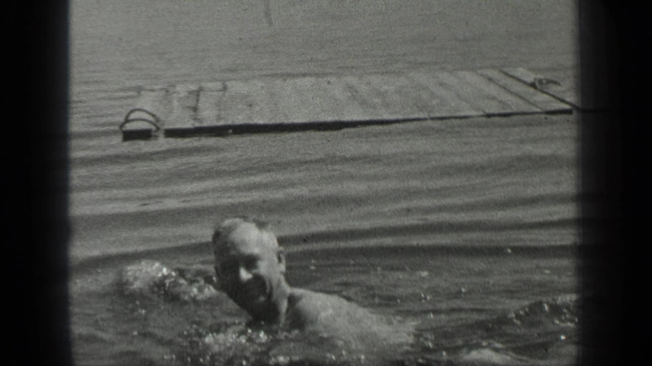 A man swims low in the frame at Long Lake, Canada, while the weathered wooden pier stretches across the background.