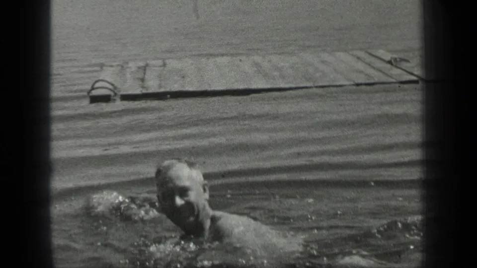 A man swims low in the frame at Long Lake, Canada, while the weathered wooden pier stretches across the background.