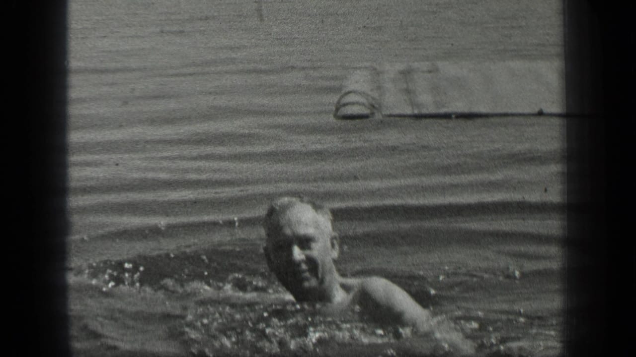 The adult swimmer moves toward the camera at Long Lake, Canada, with splashing water and a wooden pier in the background.