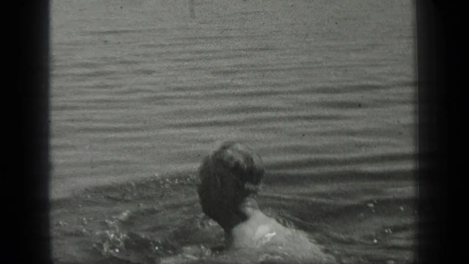 The swimmer turns away from the camera in Long Lake water, with a small dock visible beyond him.