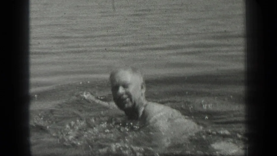 An older man faces the camera while swimming in metadata-supported 1939 Long Lake footage.