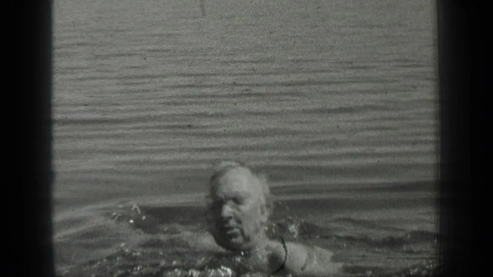 An older swimmer crosses the frame in Long Lake, Canada, with only water and ripples around him.