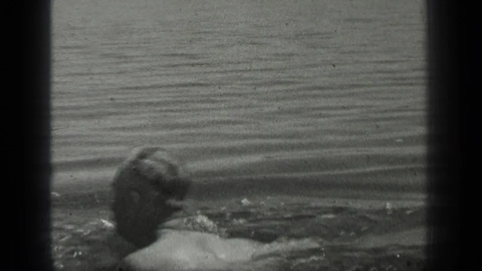 The man is seen from behind while swimming in Long Lake, with his head low in the water and ripples around him.