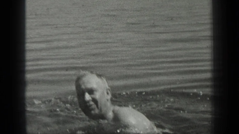 Adult man swims in Long Lake, Canada, in 1939 black-and-white 8mm home-movie footage, with his head and shoulders above the water.