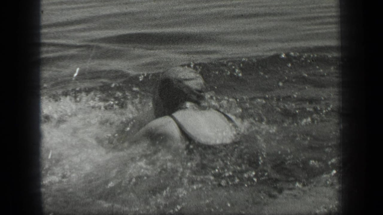 In 1939 Long Lake, Canada footage, a woman in dark swimwear swims through rippling lake water, seen from behind.