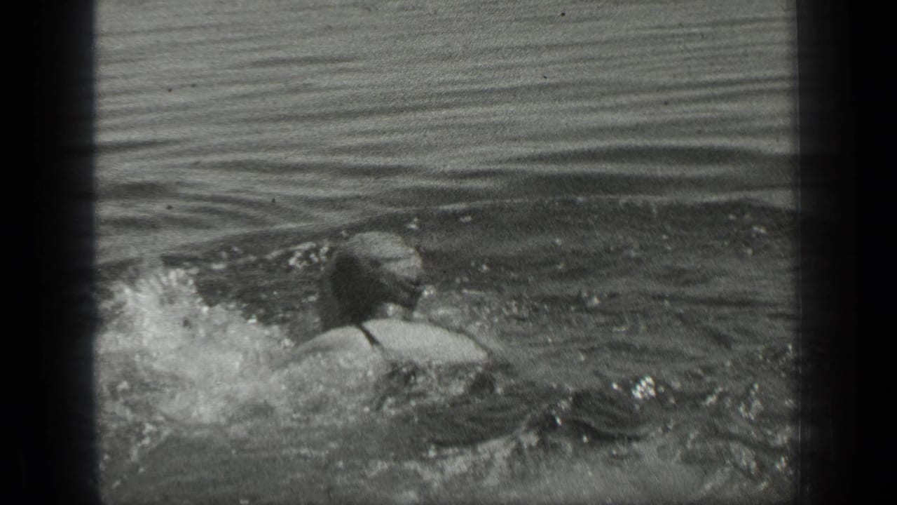 The 1939 Long Lake, Canada home-movie frame shows a woman swimming away from the camera in dark swimwear.