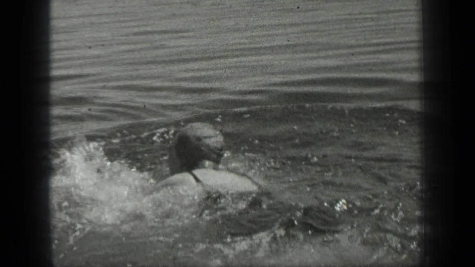The 1939 Long Lake, Canada home-movie frame shows a woman swimming away from the camera in dark swimwear.