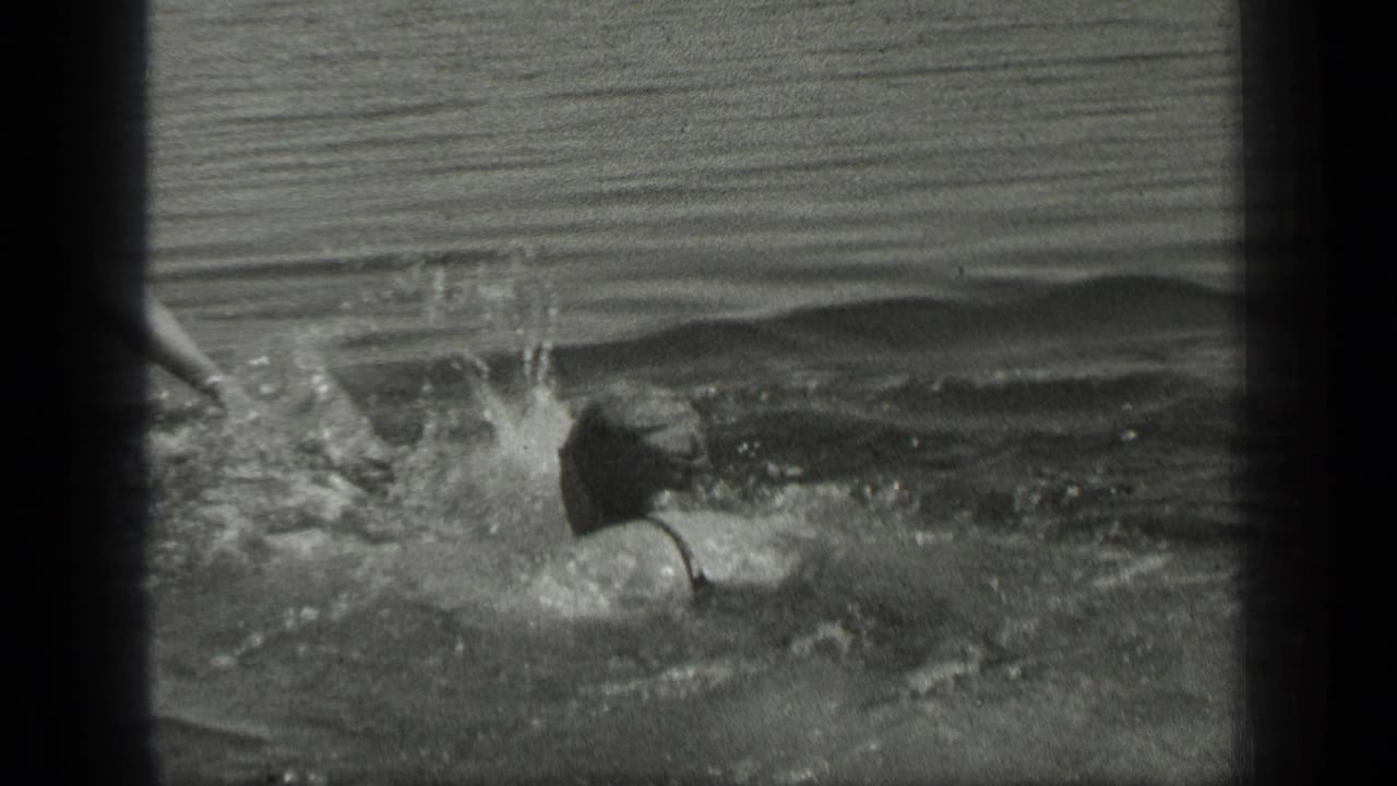 A woman in dark swimwear remains low in the water as splashes rise nearby in the Long Lake, Canada scene.