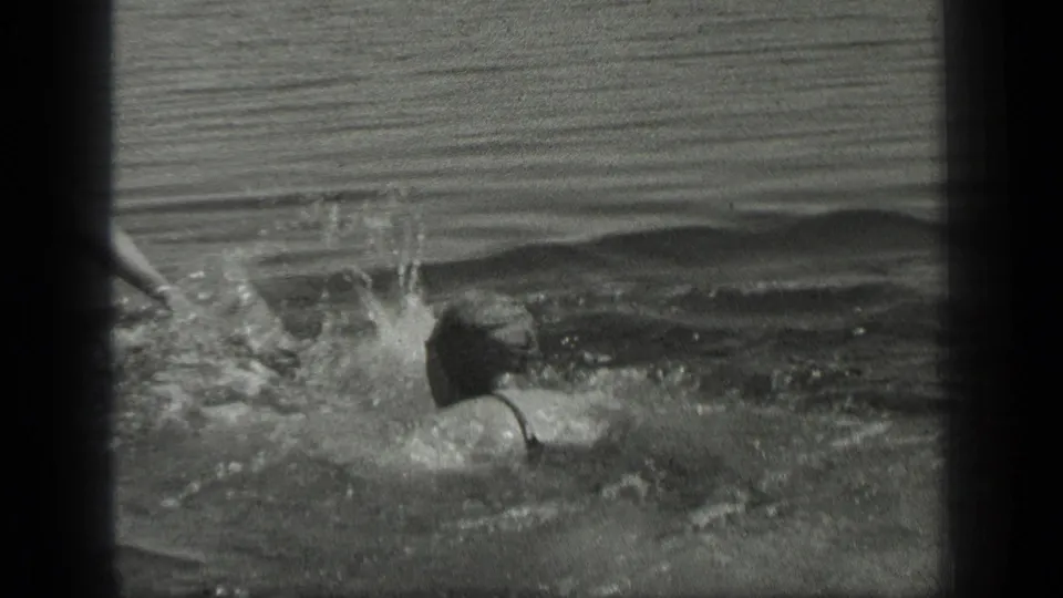 A woman in dark swimwear remains low in the water as splashes rise nearby in the Long Lake, Canada scene.