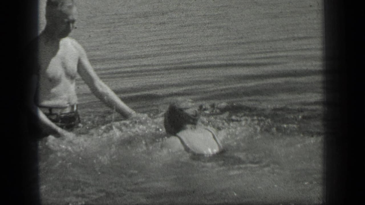 At Long Lake, Canada in 1939, a man in swim trunks stands waist-deep as a woman swims toward his outstretched hand.