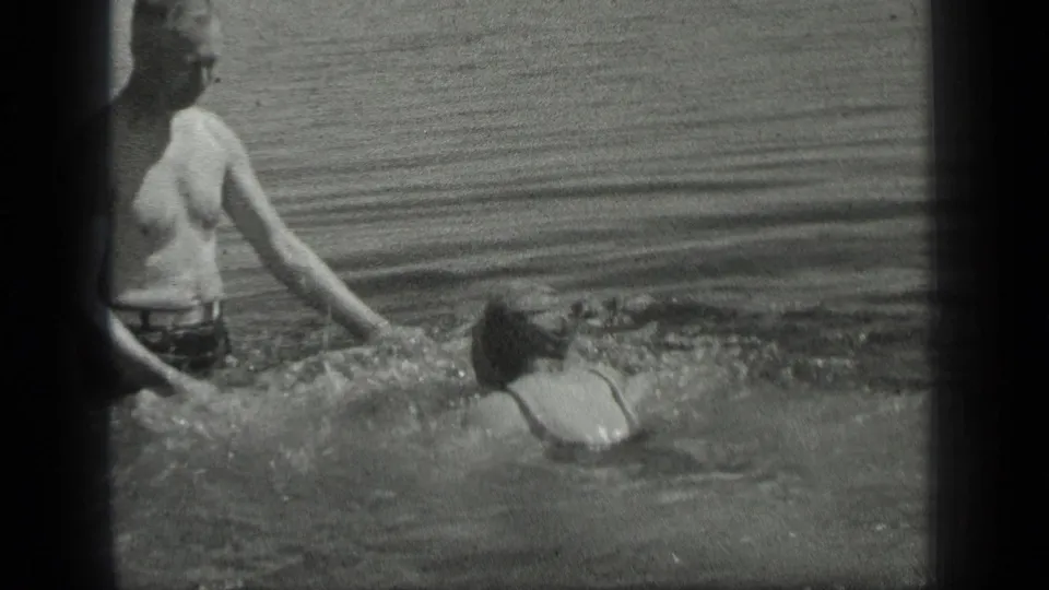 At Long Lake, Canada in 1939, a man in swim trunks stands waist-deep as a woman swims toward his outstretched hand.