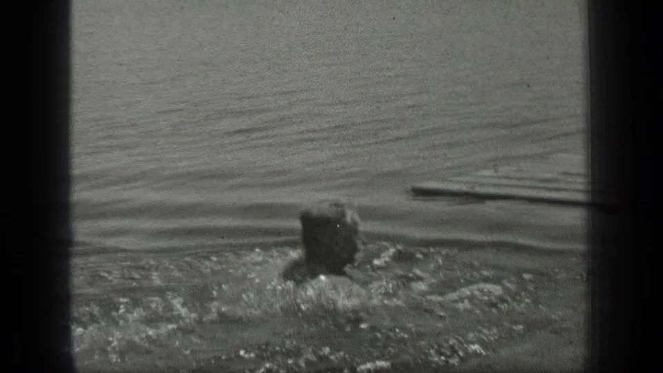 The swimmer continues across Long Lake, Canada, with a narrow wooden board or dock edge visible ahead in the water.