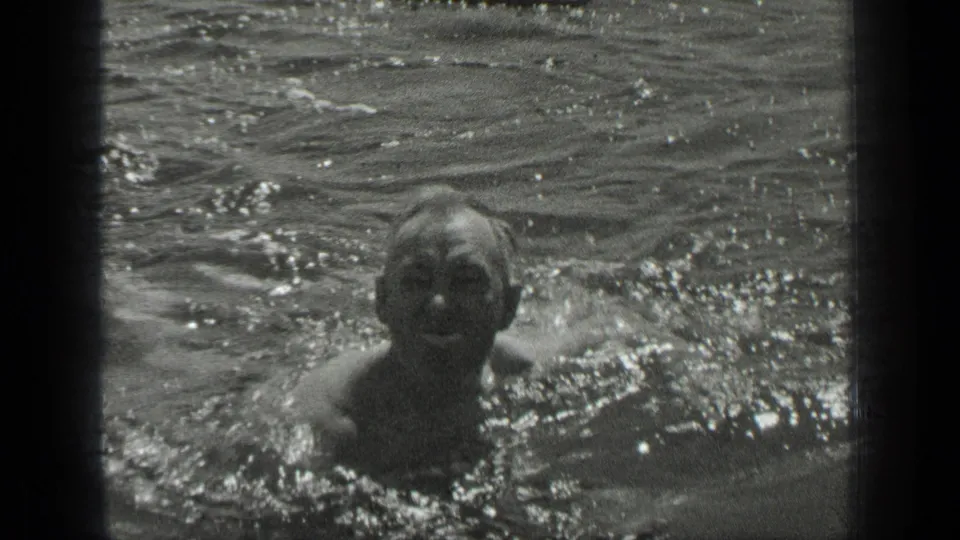 A swimmer faces the camera in 1939 Long Lake footage, with water splashing around the upper body.