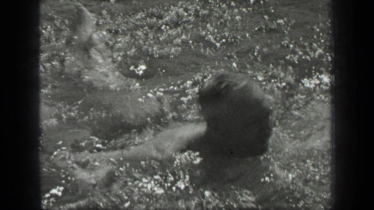 The swimmer remains low in the water as splashes break across the frame in the Long Lake home-movie shot.