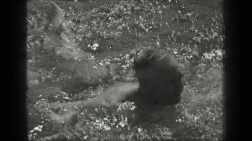 The swimmer remains low in the water as splashes break across the frame in the Long Lake home-movie shot.