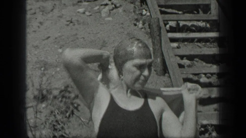 At Long Lake, Canada, the woman stands near shoreline steps in a one-piece bathing suit and swim cap.