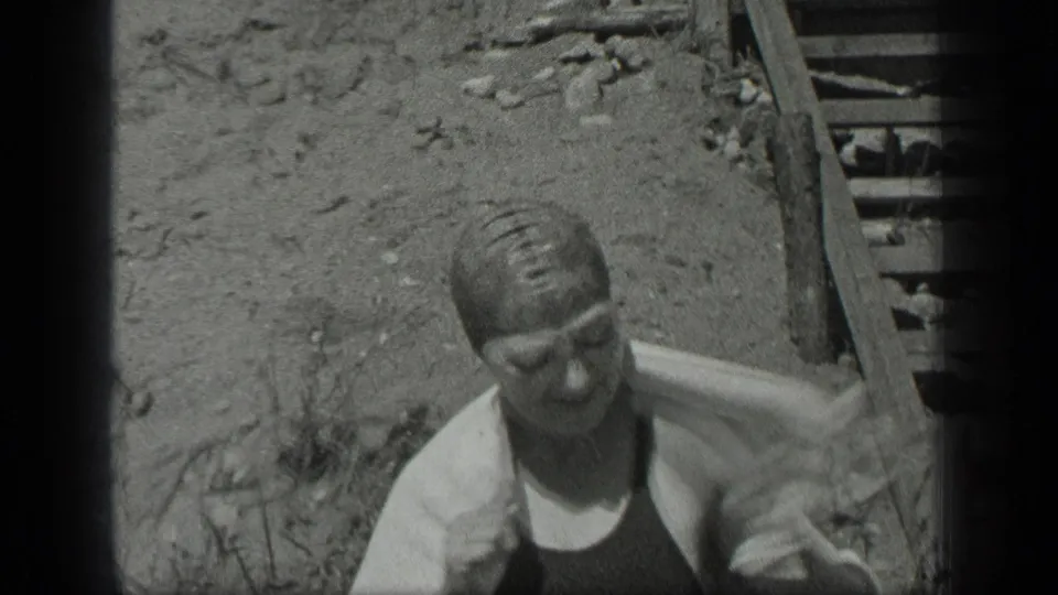 The woman towels off by the shoreline steps at Long Lake, Canada, in black-and-white 8mm footage from 1939.