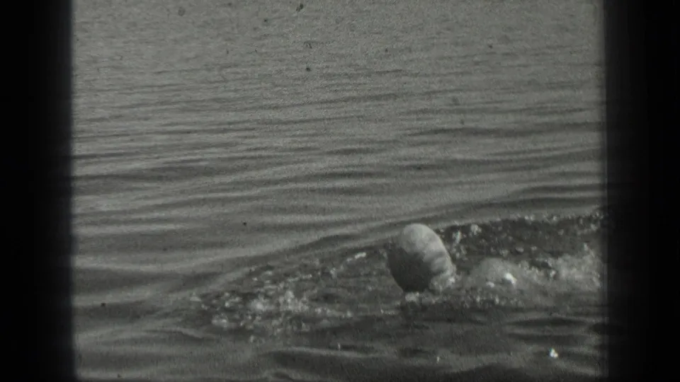 1939 Long Lake, Canada frame with a swimmer in a cap moving through calm lake water, seen from an amateur shoreline perspective.