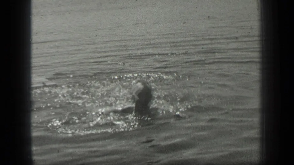 A woman swims through Long Lake water in a grainy 1939 black-and-white home-movie frame.